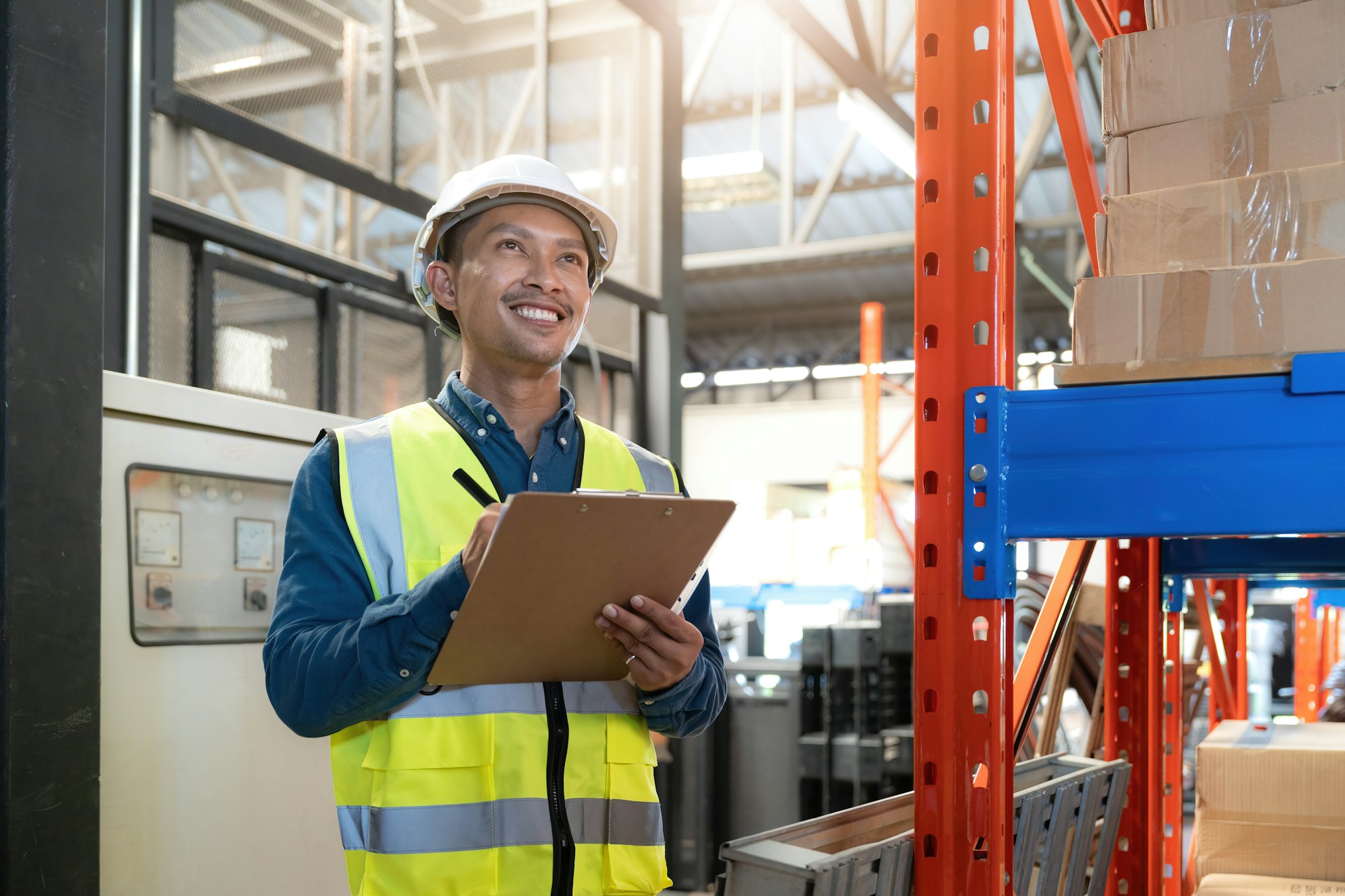 Portrait An Asian warehouse worker in a blue security suit holding clipboard working at store